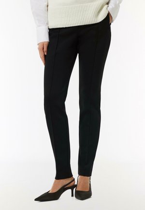 Black tailored trousers with a slim fit, featuring side pockets and contrasting stitching. Paired with black slingback heels.