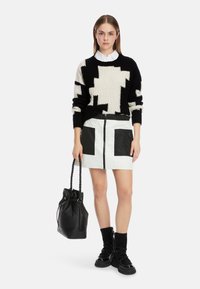 Schwarzer und cremefarbener gemusterter Strickpullover, weißer steppierter Minirock mit schwarzen Taschen, schwarze Bucket-Bag und schwarze Stiefeletten mit Reißverschlüssen.