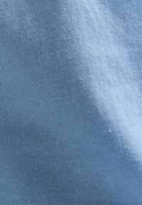 Světle modrá texturovaná látka s jemným vzorem tkaní, vyrobená z přírodních vláken, vykazující malé variace v odstínu a textuře.