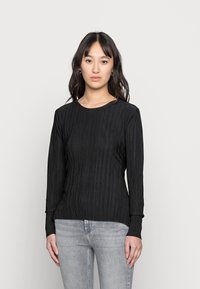 Top preto de manga longa com textura canelada vertical, decote redondo e punhos ajustados. Combinado com uns jeans cinza claro.