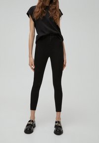Black T-shirt with rolled sleeves, paired with black skinny jeans and black loafers featuring a gold chain detail. Smooth texture throughout.