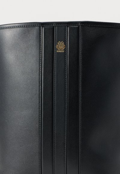 Μαύρο δερμάτινο μποτάκι με κάθετα ραμμένα πάνελ και μικρό χρυσό λογότυπο Bally κοντά στο πάνω κέντρο.