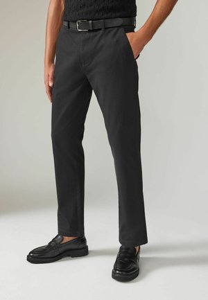 Pantalones negros de tejido entrelazado con frente plano, bolsillos laterales y corte ajustado. Combinados con mocasines negros de suela gruesa.