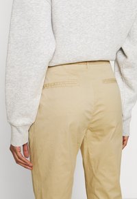 Beiga byxor i lätt tyg, med bakfickor och rak silhuett, i kombination med en ljusgrå sweatshirt.