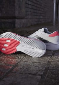 Witte hardloopschoenen met een gestructureerde bovenkant en rode accenten. De zool heeft groeven voor grip en een lichtgewicht ontwerp, gelabeld "ADIZERO."