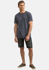 T-shirt di cotone grigio scuro con scollatura rotonda, abbinato a pantaloni corti in denim scuro. Il modello indossa scarpe marroni con lacci.