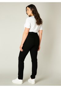 Zwarte high-waisted jeans met een textuurafwerking, gecombineerd met een aansluitend wit t-shirt en witte sneakers. Zichtbare stiksels en achterzakken.
