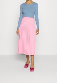 Světlomodrý žebrovaný top s dlouhými rukávy spojený s růžovou plisovanou sukní střední délky a růžovými sandály na blokovém podpatku. Hladká textura a přiléhavý střih.