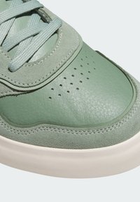 Zelené tenisky s texturovaným svrškem z kůže a semiše, kulatou špičkou, větracími otvory a světlou gumovou podrážkou.