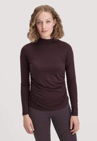 Dunkelviolettes Langarm-Turtleneck-Shirt mit enganliegendem Design, das eine geraffte Textur an der Taille und Raglanärmel aufweist. Weicher Stoff.