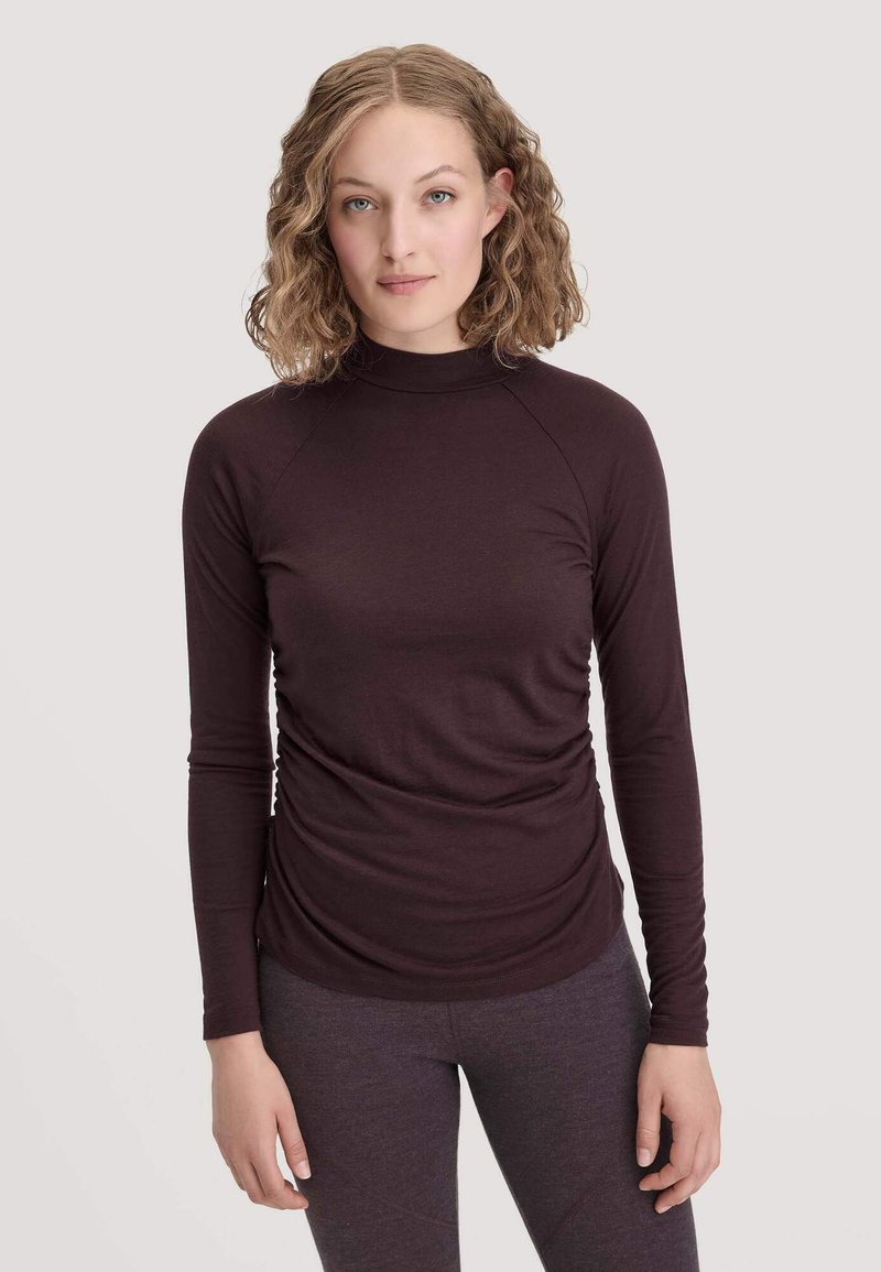 Dunkelviolettes Langarm-Turtleneck-Shirt mit enganliegendem Design, das eine geraffte Textur an der Taille und Raglanärmel aufweist. Weicher Stoff.