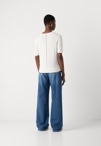 Haut en tricot blanc à manches courtes avec un détail de fermeture éclair au dos, associé à un jean bleu ample avec des jambes larges et des coutures visibles.