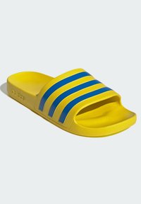 Chanclas amarillas con suela texturizada, que presentan tres rayas azules en la tira y un logotipo en relieve en el lateral. Diseño ligero.