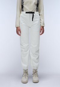 White waterproof pants with elastic cuffs and black adjustable waistband. Paired with beige lace-up boots. Smooth, glossy texture.