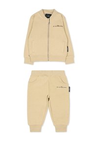 Ensemble de surv êtement en coton beige comprenant une veste bomber zippée avec des poches latérales et un pantalon fuselé assorti avec des poignets élastiques et des accents de poches avant.