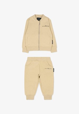 Beige katoenen trainingsoutfit met een ritssluiting bomberjack met zijzakken en bijpassende tapered broek met elastische boorden en accentzakken aan de voorkant.