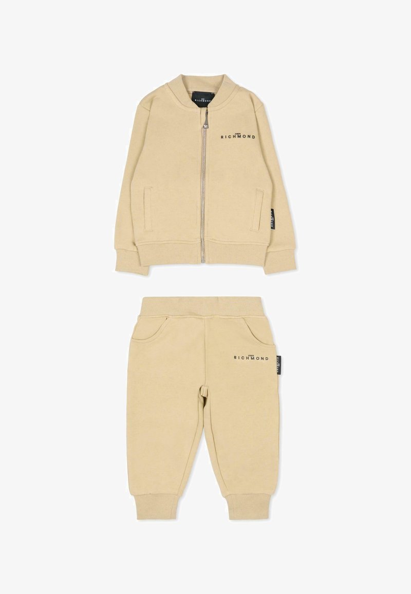 Tuta in cotone beige composto da una giacca bomber con zip e tasche laterali, abbinato a pantaloni tapered con polsini elasticizzati e accenti di tasca frontale.