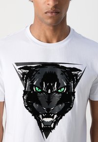 Camiseta de algodón blanca con un gráfico de pantera negra con ojos verdes, enmarcada dentro de un diseño triangular negro. Manga corta y escote redondo.