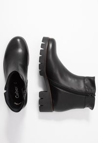 Bottes de cheville en cuir noir avec une semelle épaisse texturée, fermeture éclair sur le côté, finition lisse et bout arrondi. Présente un marquage subtil à l'intérieur.