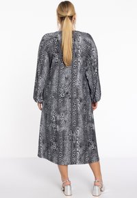 Robe en imprimé serpent noir et blanc avec des manches longues, longueur mi-mollet, coupe décontractée et un col rond. Sandales à talons argentés visibles.