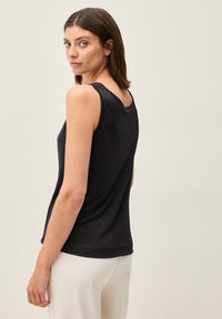 Top senza maniche nero realizzato in un tessuto morbido, con scollatura rotonda e vestibilità rilassata, indossato con pantaloni chiari. Vista posteriore mostrata.