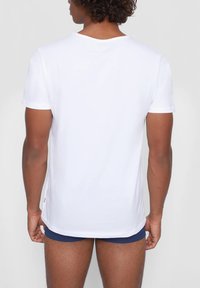 White short-sleeve T-shirt, crew neck, made of soft fabric. Features a straight hem and small logo accent at the bottom.