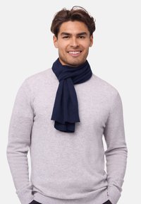 Marineblå strikket tørklæde hængt om halsen, med en blød tekstur og ribbede kanter, parret med en lys grå sweater.