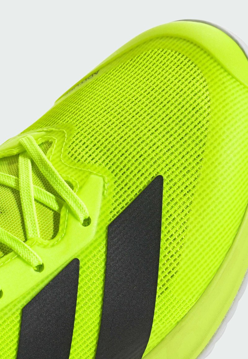 Baskets de sport jaune vif avec un dessus en maille, une surface texturée, des rayures d'accent noires et des lacets plats. Semelle blanche incurvée.