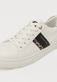 Hvite sneakers med teksturert lær, med svarte og leopardmønstrete detaljer og kontrasterende kremfargede lisser. Rund tå og gummisåle.