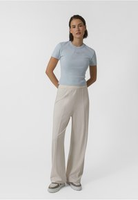 T-shirt ribbed bleu clair à manches courtes, associé à un pantalon large beige. Les chaussures présentent un accent à motif et une épaisse semelle blanche.