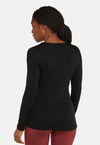 Camisa negra de mangas largas, confeccionada con un material suave, con un escote redondeado y detalles en las costuras de los hombros, combinada con leggins rojos.