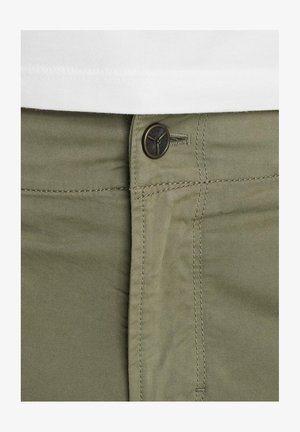 Olivengrønne bukser med en glat tekstur, der har en metalknap i taljen og synlige sømme langs sømmene.