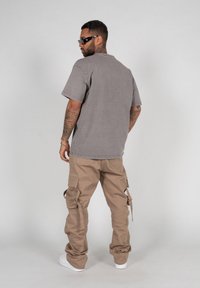 Gray oversized T-shirt with a crew neck, paired with tan cargo pants featuring multiple pockets and adjustable straps, worn with white sneakers.