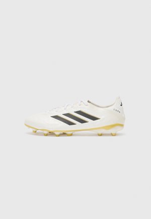 Chaussure de football blanche dotée de trois rayures noires, d'un upper texturé et de crampons jaunes. Le design comprend un motif subtil et un détail de logo.