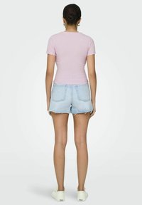 Světle růžové proužkované tričko s krátkým rukávem, spárované s džínovými šortkami světle modré barvy se třepeným lemem a bílými teniskami s černými logovými akcenty.