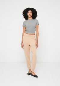 Maglietta grigia corta in cotone morbido, abbinata a pantaloni jogger color beige con dettagli a strisce laterali. Ballerine nere completano l'outfit.