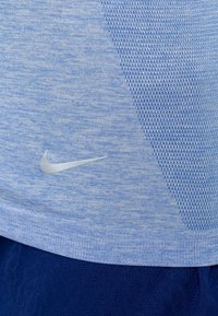Ljusblå Nike träningsskjorta med texturerad tyg, mesh-detaljer och en diskret logotyp nederst till höger. Slätt och lätt material.
