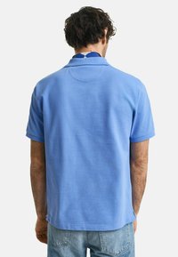 Kortärmad pikétröja i ljusblå bomull med krage, slät textur och en rundad ryggdetalj.