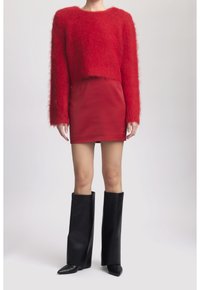 Un pull rouge moelleux court à manches longues associé à une jupe mini rouge et des bottes en cuir noires montantes avec des talons pointus.