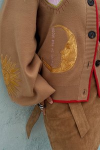 Brun strikket cardigan med intrikate gull broderinger av sol og måne, med ribbestrikket kant og utringning med røde detaljer og svarte knapper.