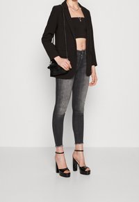 Blazer negro sobre una parte superior negra corta, combinado con jeans ajustados grises. Accesorios con un pequeño bolso negro y tacones de plataforma negros.