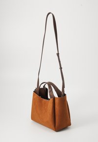 Brun semsketotebag med en strukturert design, doble topphåndtak og en justerbar skulderreim. Glatte lærdetaljer er til stede.