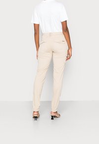 Beige cargobyxor med sidfickor, slim fit och midja i medelhöjd. Materialet verkar lätt och mjukt; kombinerat med en vit t-shirt.