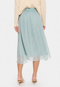 Gonna midi fluida di un verde chiaro, realizzata in tessuto trasparente con una vita elastica. Presenta un design a strati con un orlo leggermente ondulato.