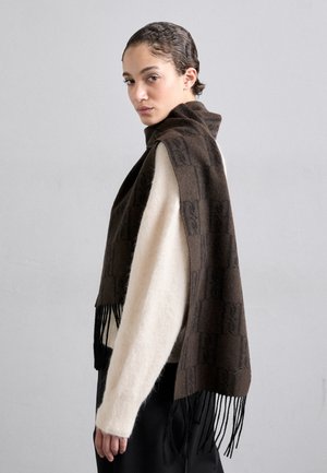 Écharpe brune à motif avec des bords frangés, fabriquée en matériau doux, drapée sur un pull de couleur claire, présentant un design moderne.