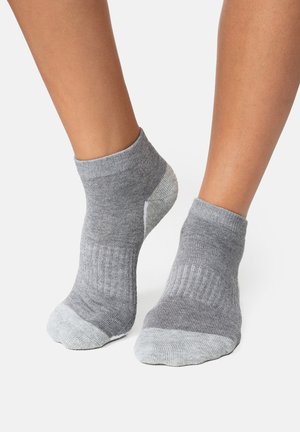 Stopy w szarych skarpetkach do kostek z jaśniejszymi, szarymi palcami i piętami na białym tle.