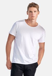 Vit t-shirt med rund halsringning, tillverkad av bomull, med korta ärmar och en avslappnad passform, bärs med mörka shorts. Minimalistisk design, slät textur.