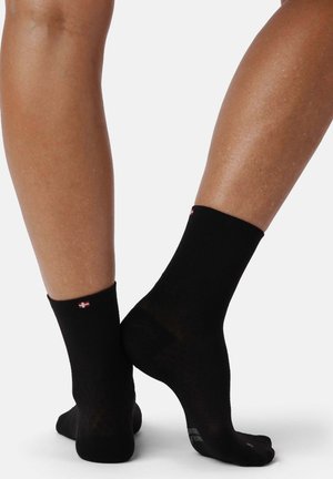 Svarta ankelsockar med ribbat mönster och en liten röd logotyp vid mudden, med en slät textur och åtsittande form.