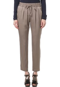 Kobieta nosząca taupe'owe spodnie na gumkę z troczkiem oraz czarną bluzkę z długim rękawem, w połączeniu z czarnymi sandałami na obcasie z odsłoniętą palcami i frędzlami.