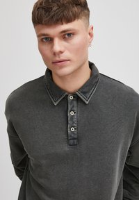Dunkelgrauer Pullover mit Kragen, der eine durchgeknöpfte Vorderseite und einen kontrastierenden Stoff hat. Weicher Stoff mit einem lässigen Schnitt.